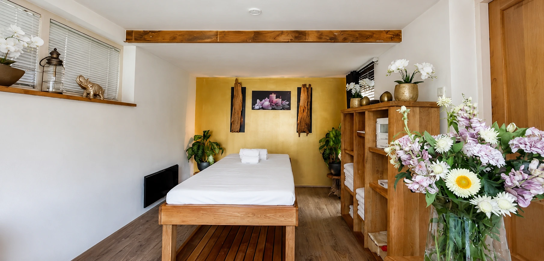 Warme behandelruimte met massagetafel en bloemen